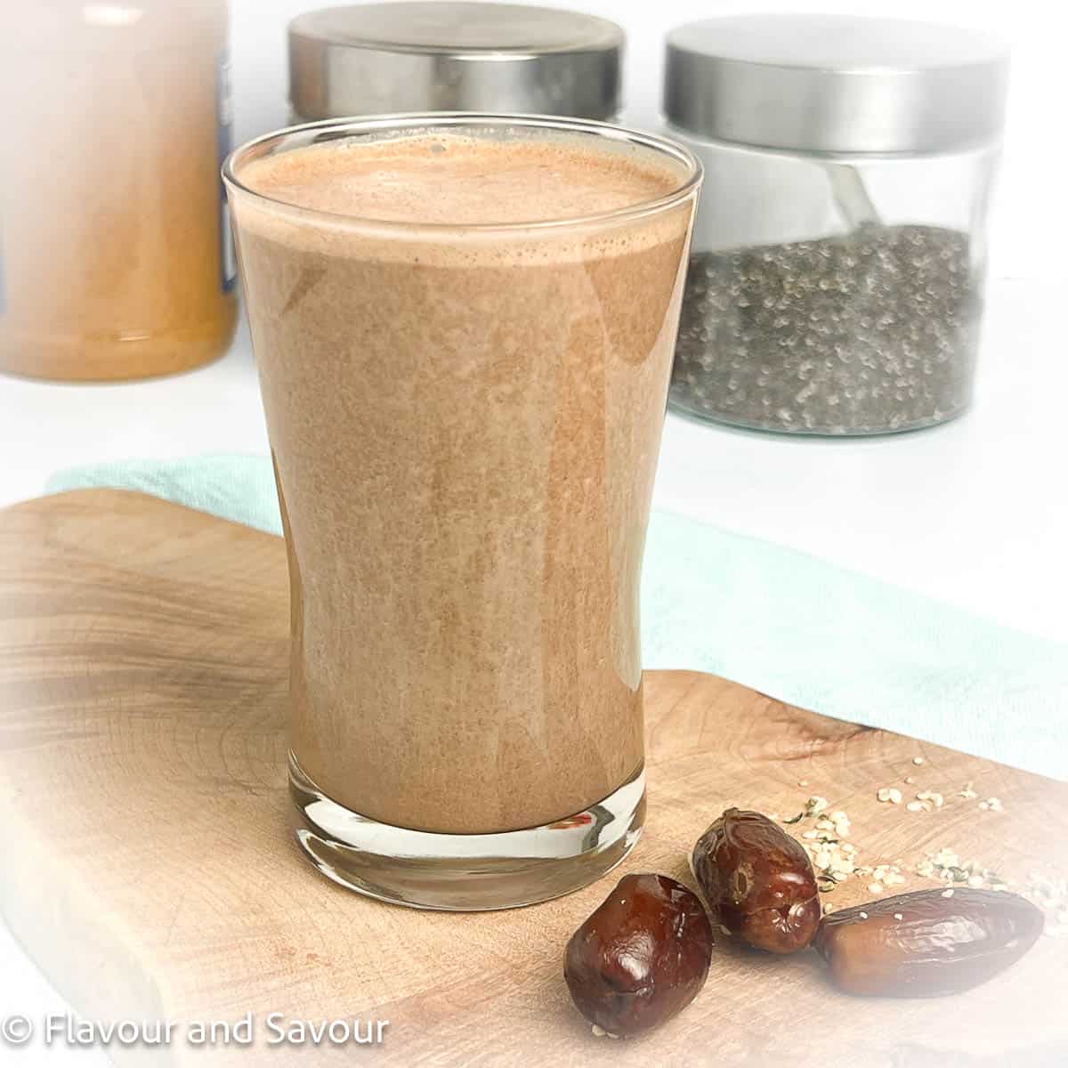 A glass of chocolate peanut butter smoothie with jars of ingredients in the background.