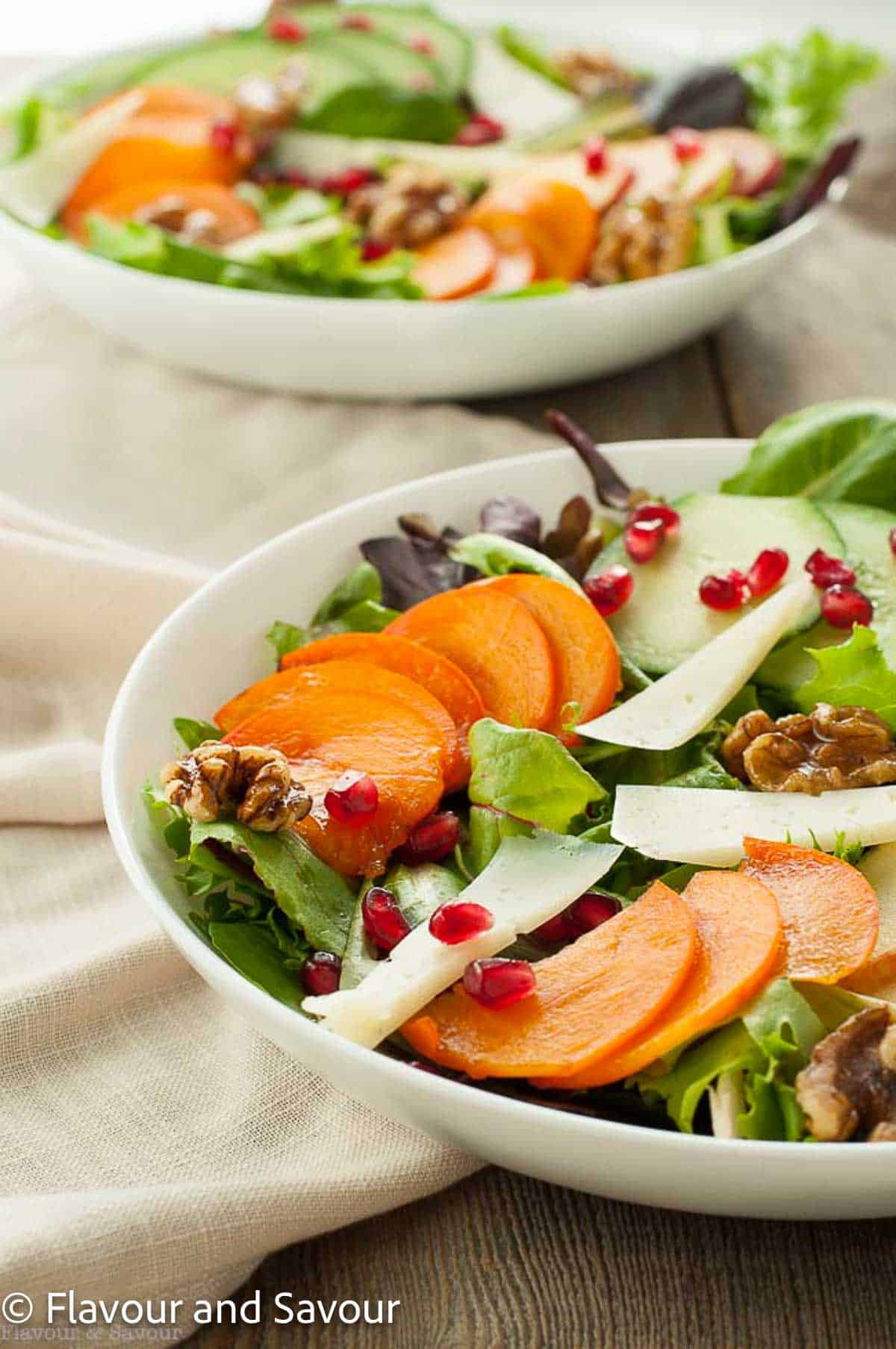 A bowl of fresh greens with sliced fruit and persimmons.