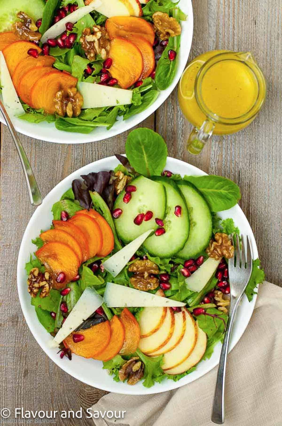 Two bowls of persimmon pomegranate salad with sliced fruit and Manchego cheese.