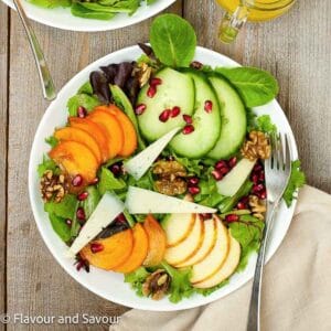 A bowl with greens, sliced persimmons, sliced apples, slice cucumbers, maple-glazed walnuts and pomegranate arils.