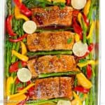 A sheet pan with glazed salmon, bell pepper strips, asparagus and lime slices.