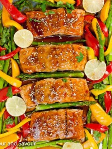 A sheet pan with glazed salmon, bell pepper strips, asparagus and lime slices.