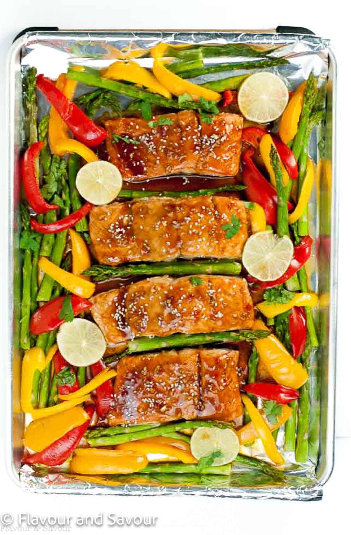 A sheet pan with glazed salmon, bell pepper strips, asparagus and lime slices.