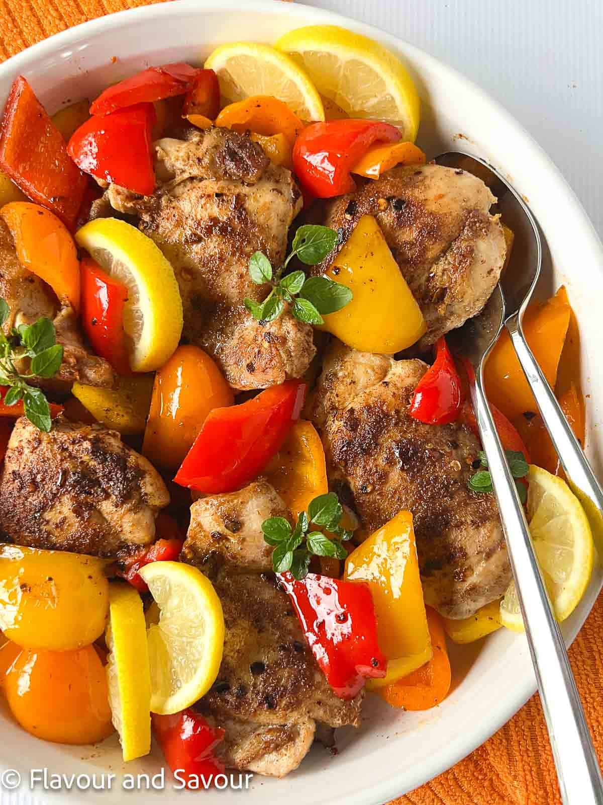 A round shallow dish with chicken thighs, colored bell peppers and lemon slices.