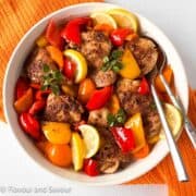 A round shallow dish with chicken thighs, colored bell peppers and lemon slices.