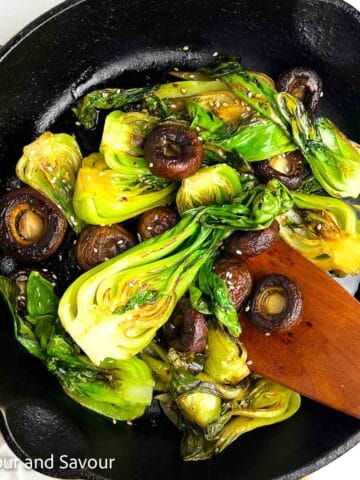 Baby bok choy and mushroom stir fry in a cast iron skillet.