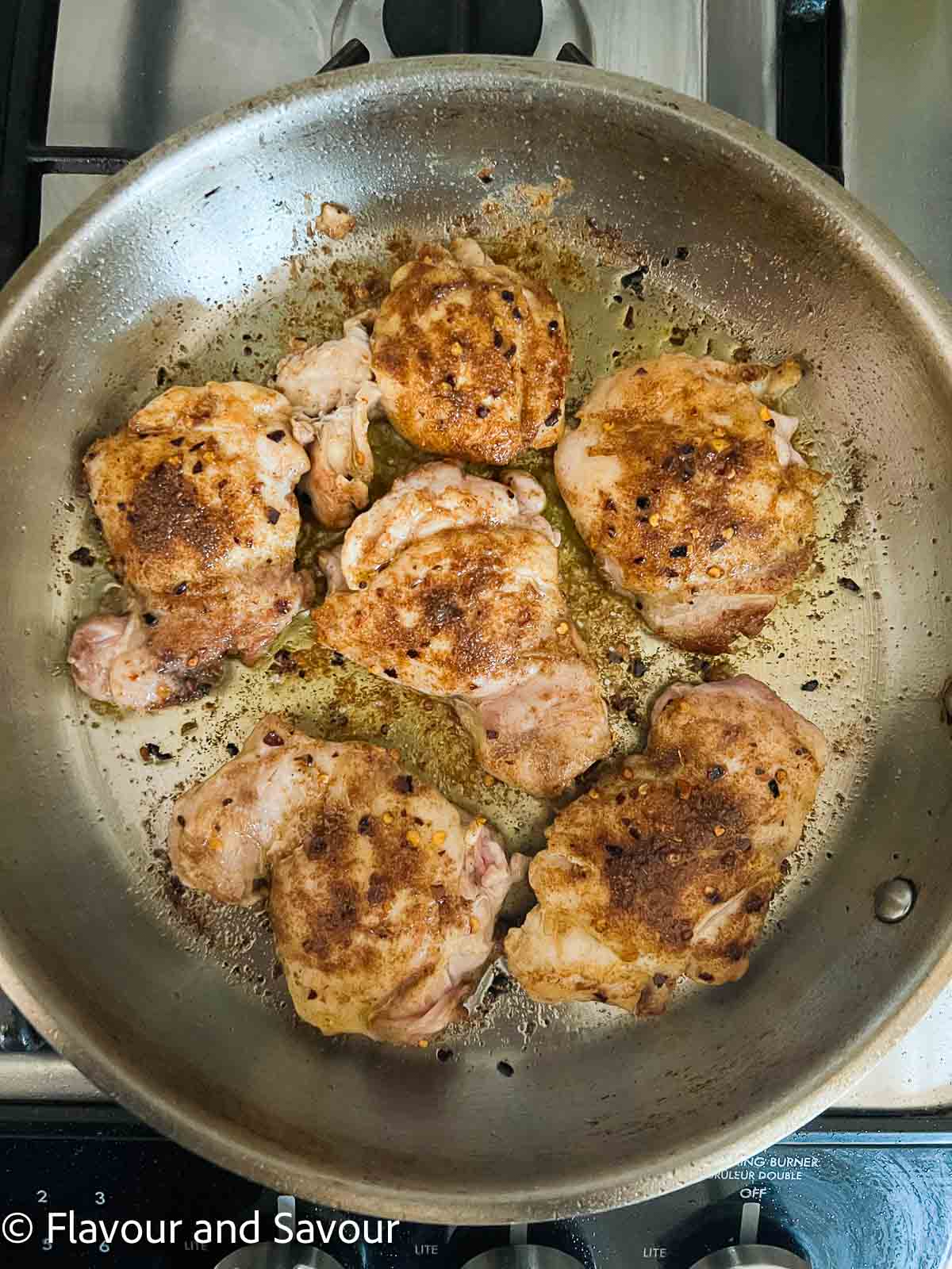 Chicken thighs with Moroccan spices browning in a skillet.