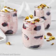 Three mini glasses of cherry coconut fool topped with chopped pistachios.