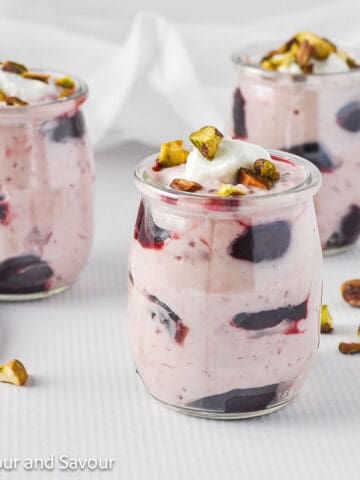 Three mini glasses of cherry coconut fool topped with chopped pistachios.