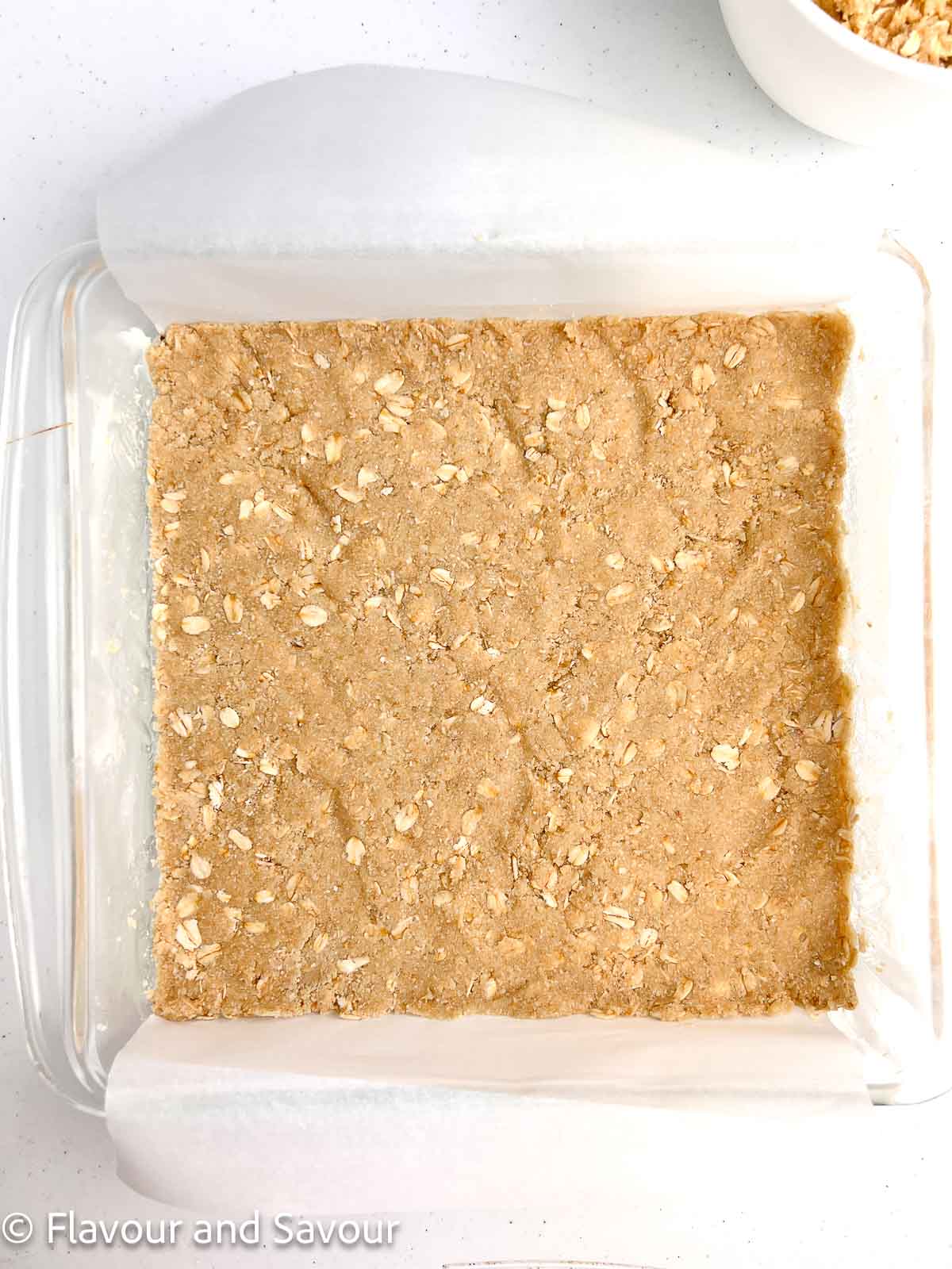 Crust mixture for cherry pie bars pressed into a glass baking pan.