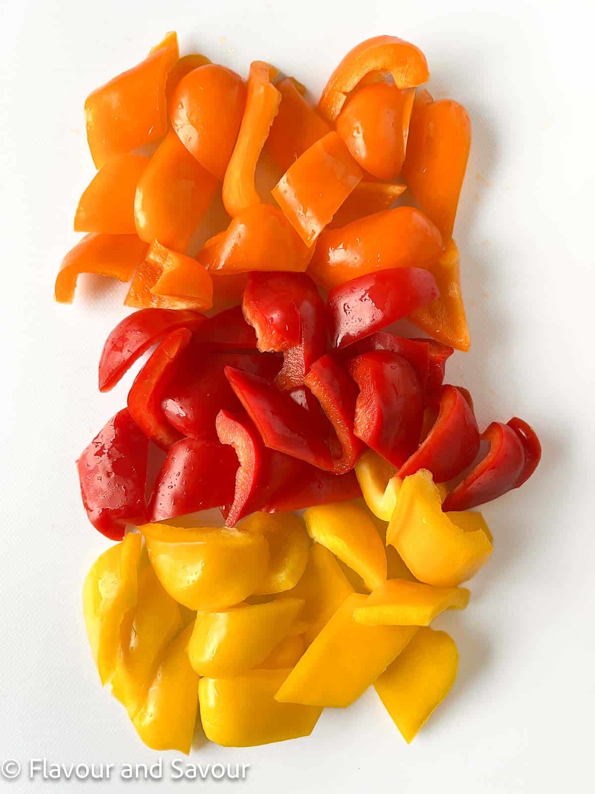 Orange, red and yellow bell peppers on a cutting board, cut into bite-sized pieces.