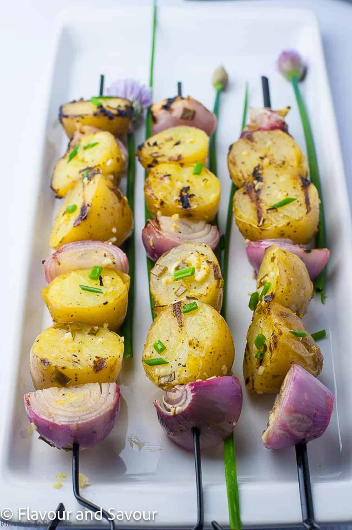 Grilled skewered potatoes and onions garnished with fresh chives.