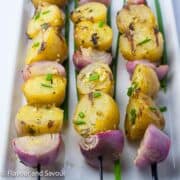 Grilled skewered potatoes and onions garnished with fresh chives.