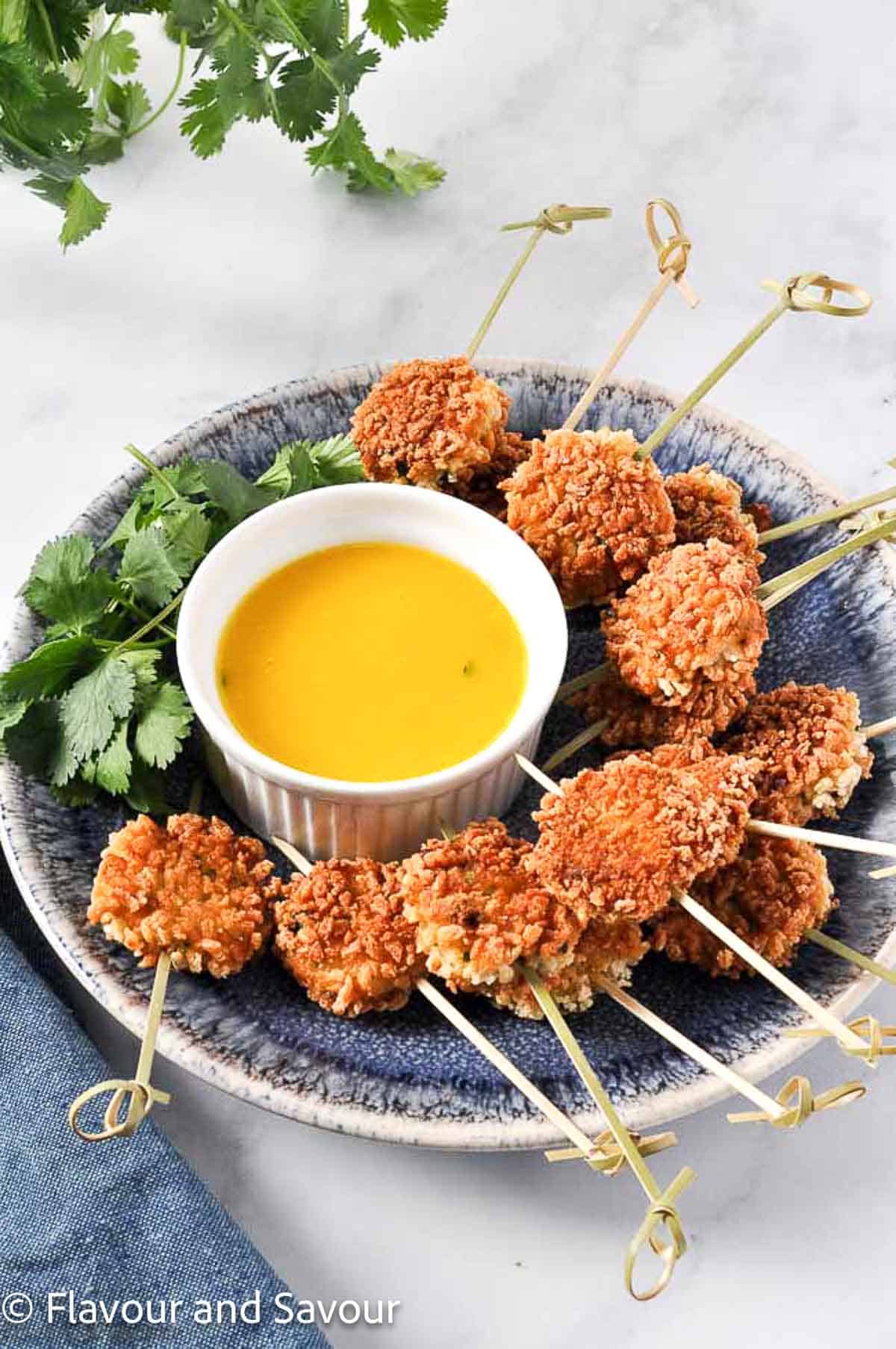 Panko coated shrimp cakes on skewers around a bowl of mango dip.