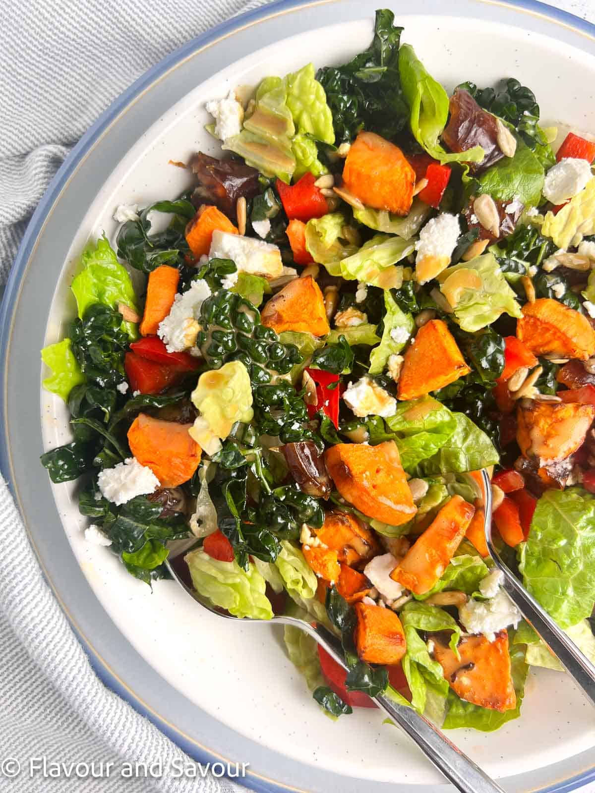 Kale Salad with air fried sweet potatoes, red pepper, feta cheese, sunflower seeds and Medjool dates in a bowl.