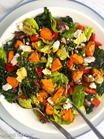 Kale Salad with air fried sweet potatoes, red pepper, feta cheese, sunflower seeds and Medjool dates in a bowl.