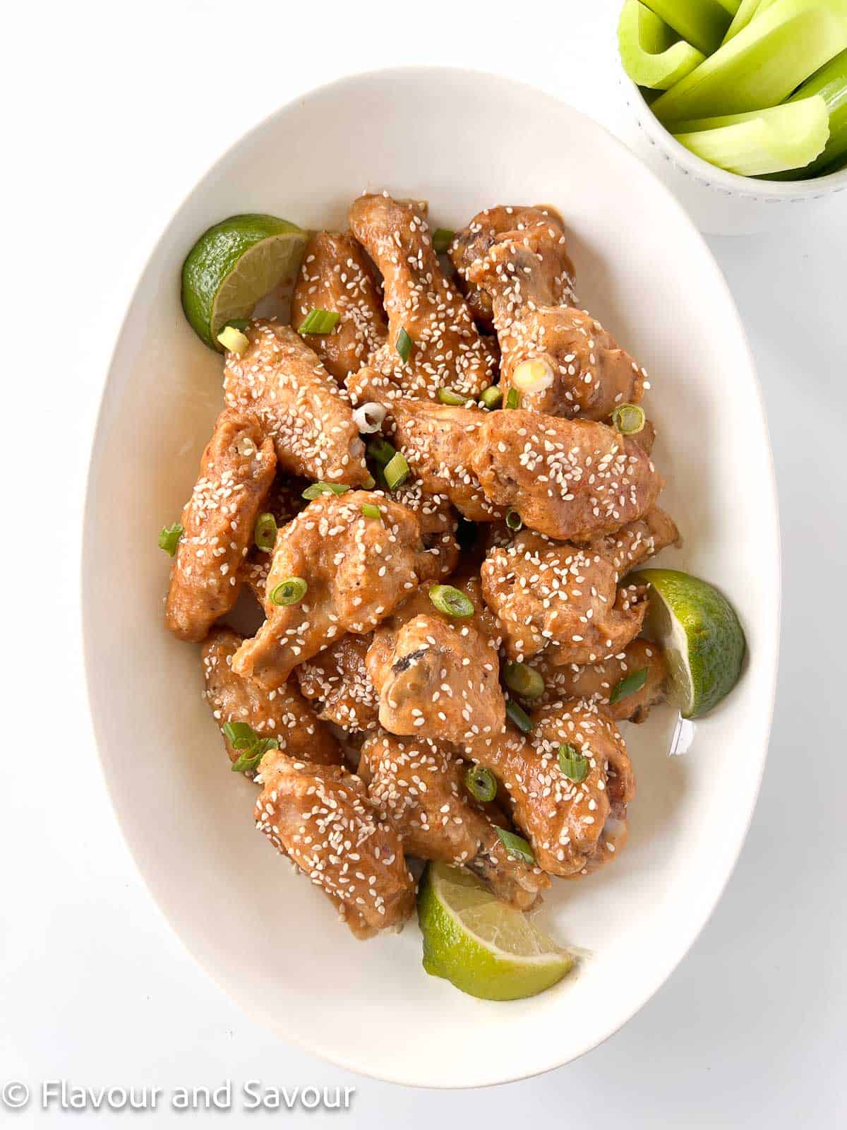 A shallow white bowl with Thai peanut chicken wings with a small bowl of celery sticks beside.