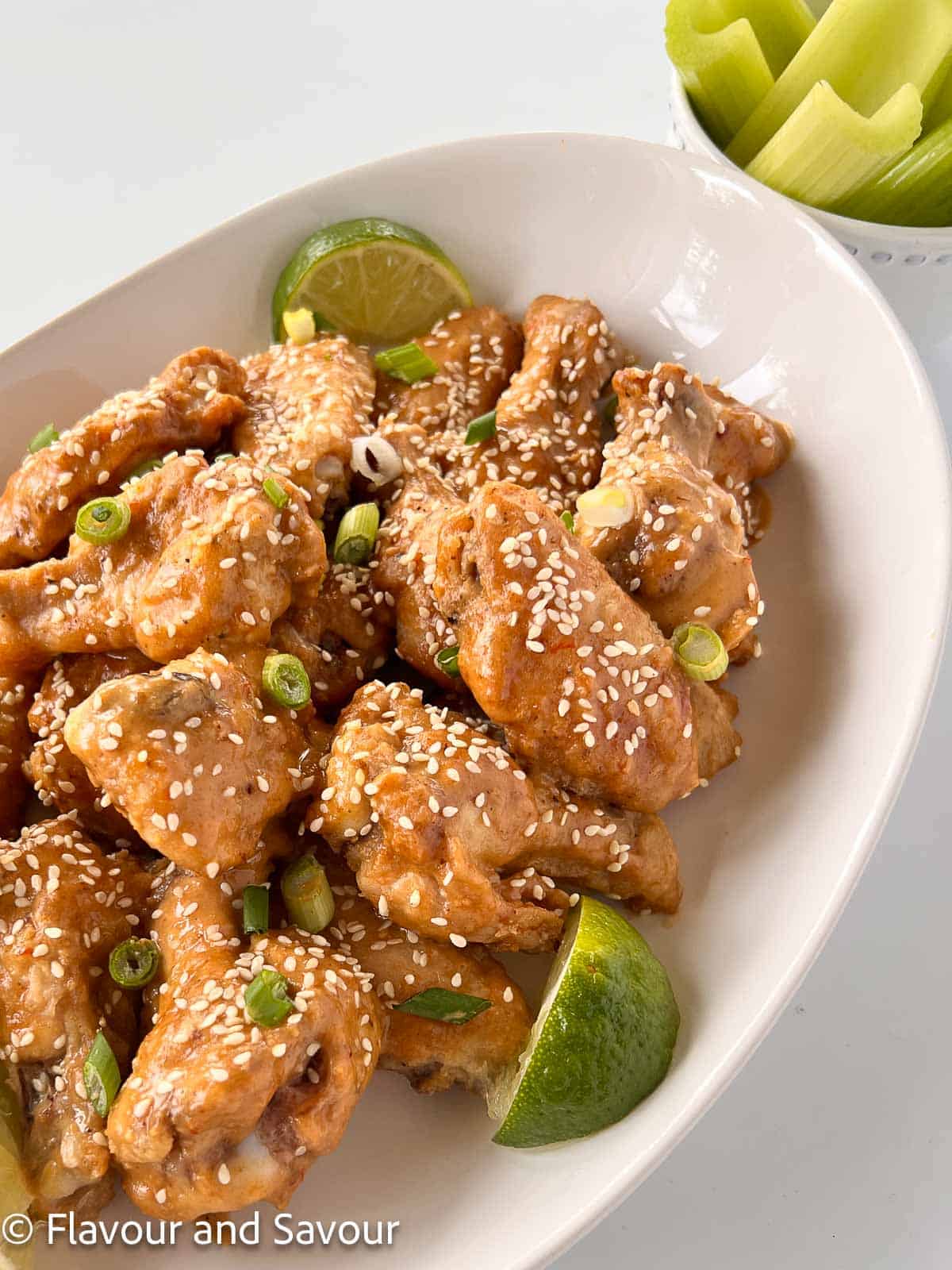 Air fryer chicken wings with peanut sauce and sesame seeds in a shallow oval bowl.