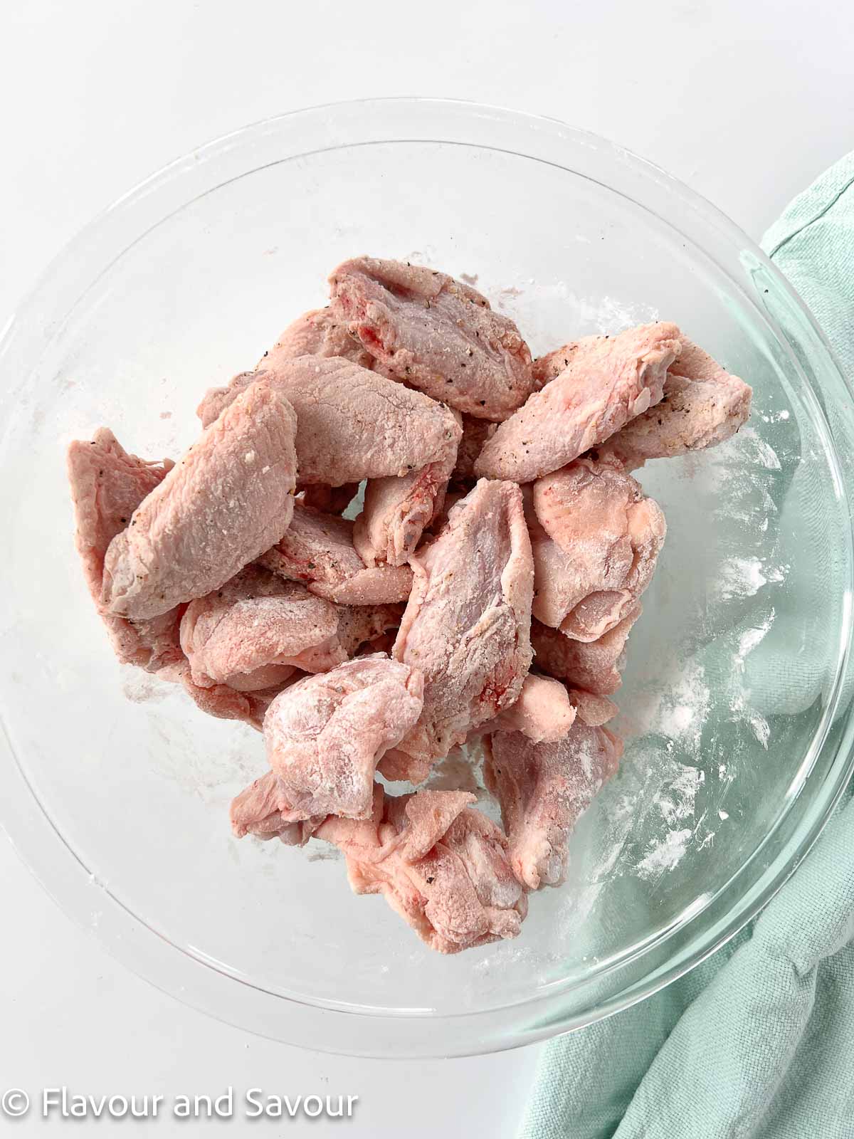 Raw chicken wings in a bowl tossed with baking powder, salt and pepper.