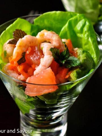 Thai-inspired shrimp salad with grapefruit, blood orange and mint leaves in a glass dish.