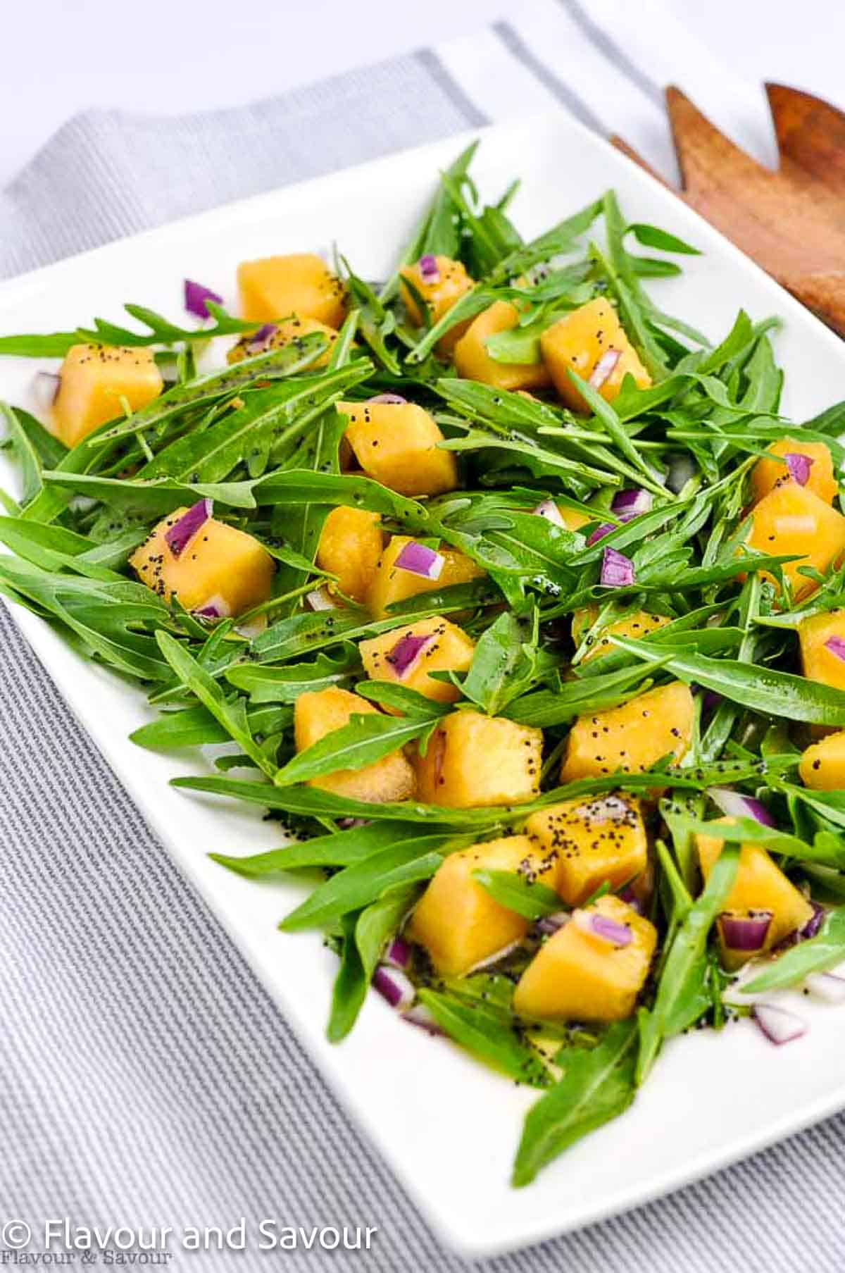 A platter with arugula leaves, cantaloupe cubes and finely chopped red onion tossed with poppyseed dressing.