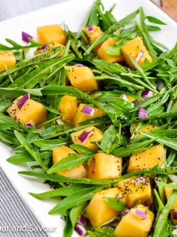 A platter with arugula leaves, cantaloupe cubes and finely chopped red onion tossed with poppyseed dressing.