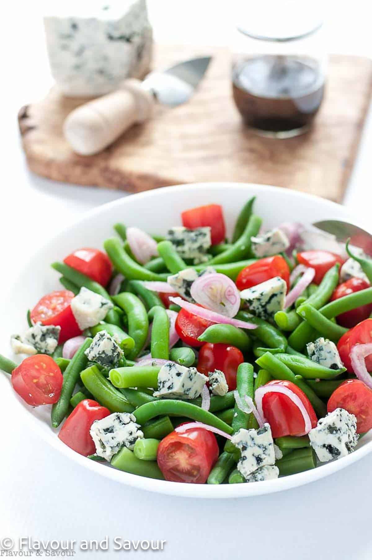 A bowl of salad with green beans, blue cheese, red onions and cherry tomatoes.