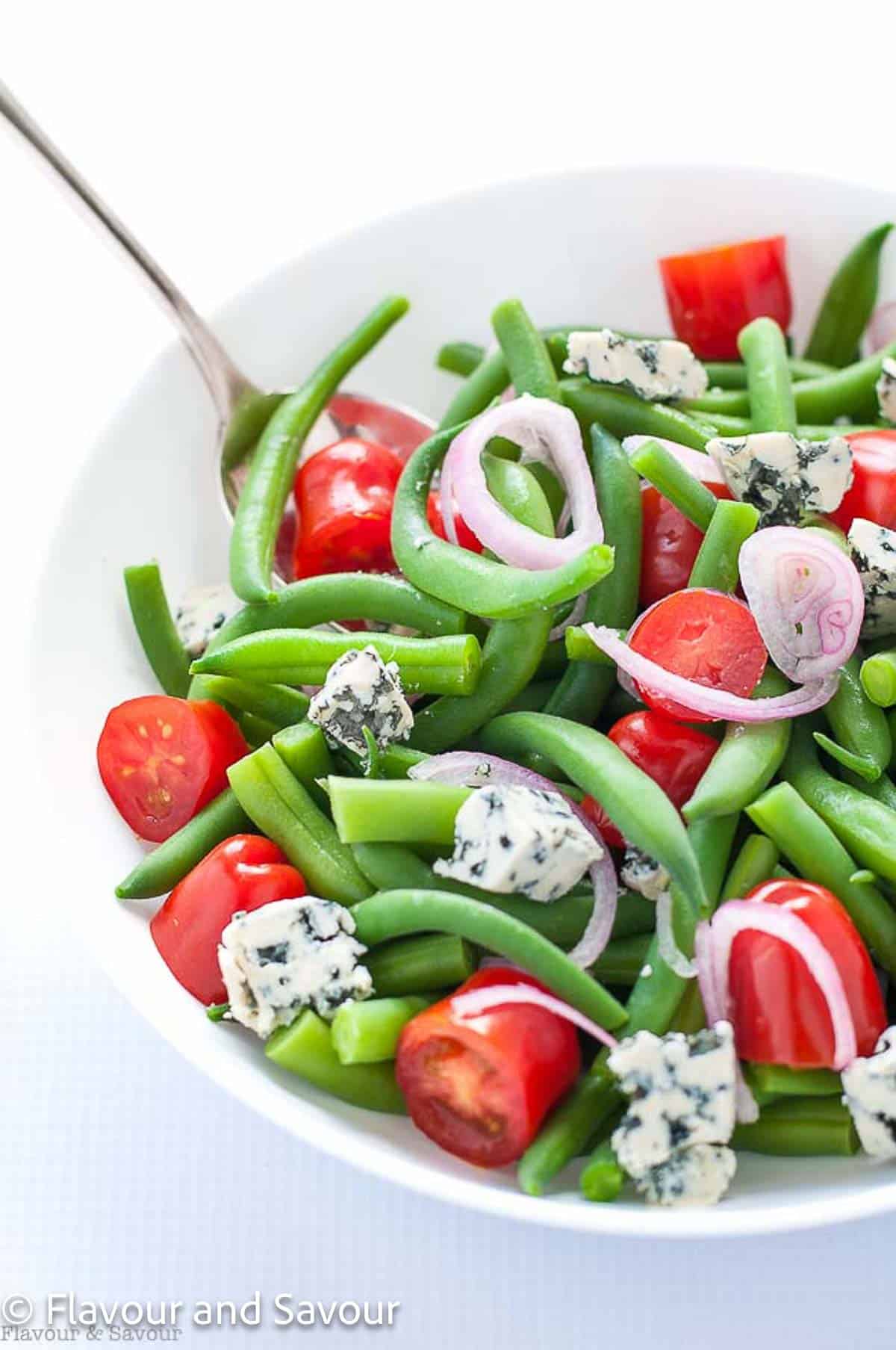 Green bean salad with blue cheese crumbles, cherry tomatoes and red onion slices.