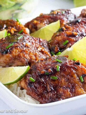 A platter of baked chicken thighs with honey chili lime seasoning served on rice with lime slices.
