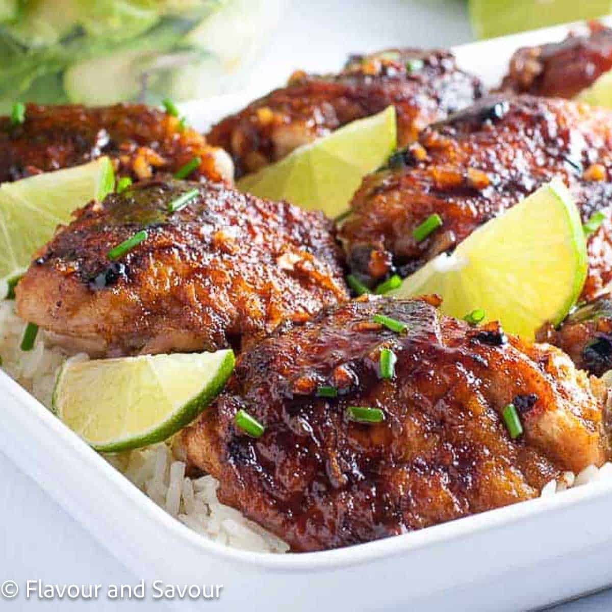 A platter of baked chicken thighs with honey chili lime seasoning served on rice with lime slices.