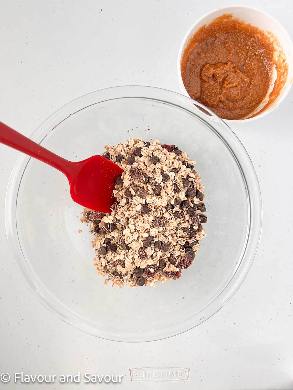 Two glass bowls, one with the dry ingredients for no-bake oatmeal energy balls and the other with a mixture of peanut butter and maple syrup or honey.