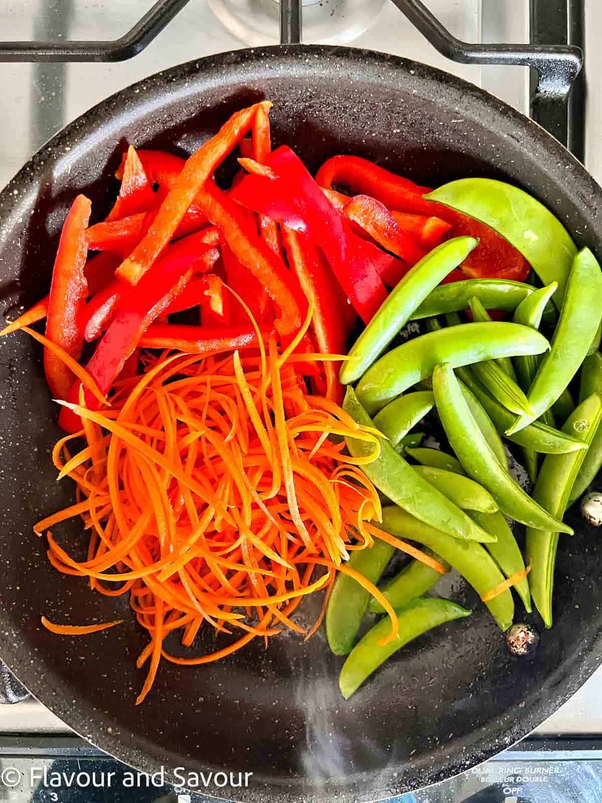 Snow peas, carrots and red pepper strips in a skillet.