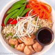 Teriyaki chicken cubes with quinoa, sugar snap peas, red pepper strips, julienned carrots, bean sprouts and a small bowl of teriyaki sauce.