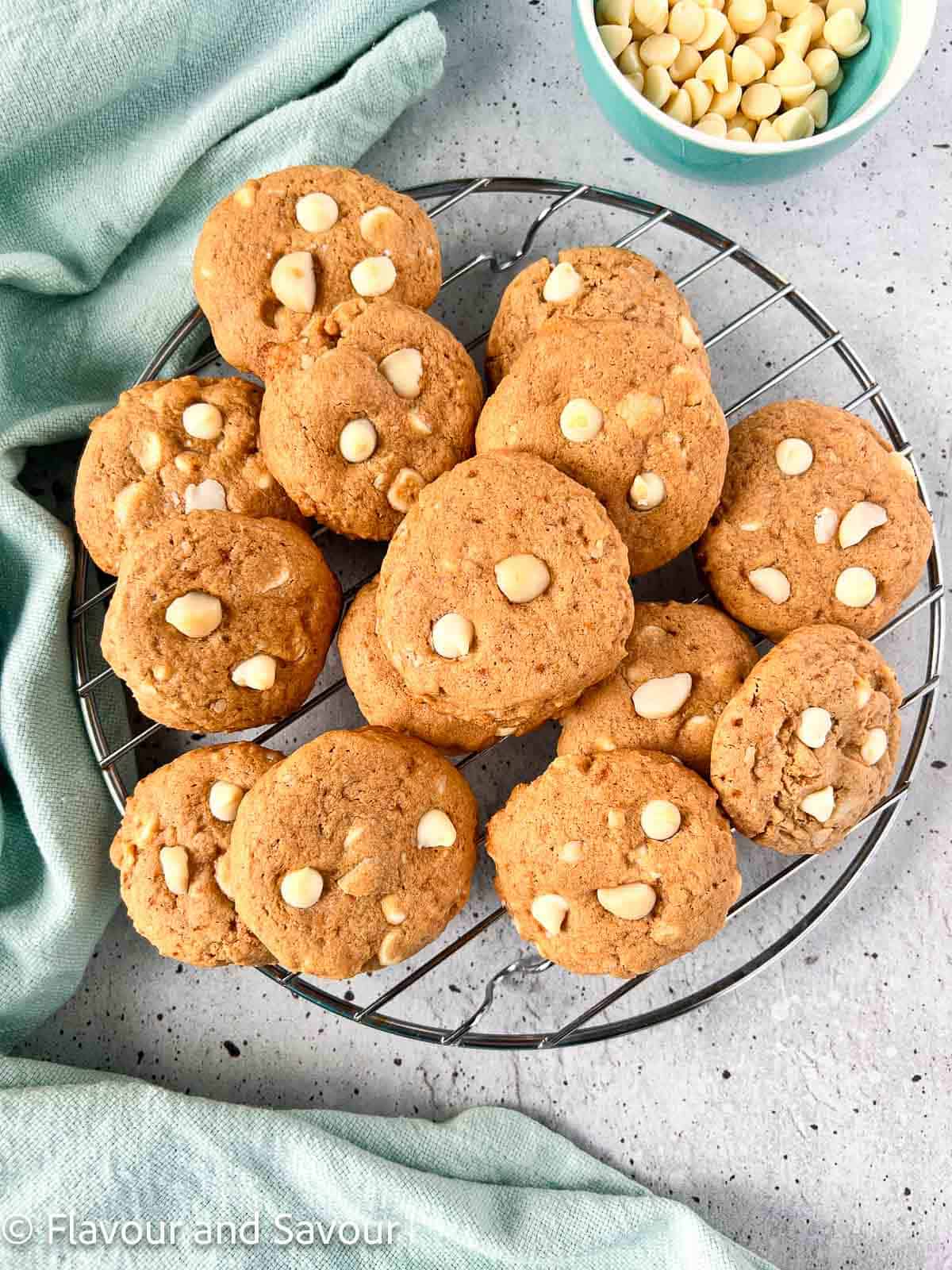 A pile of white chocolate macadamia nut cookies with a small bowl of white chocolate chips beside.