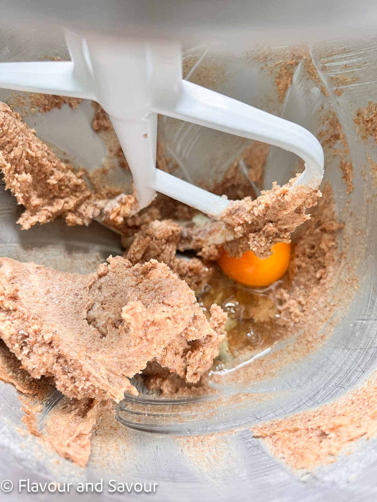 Adding an egg to creamed butter and sugar in a stand mixer.