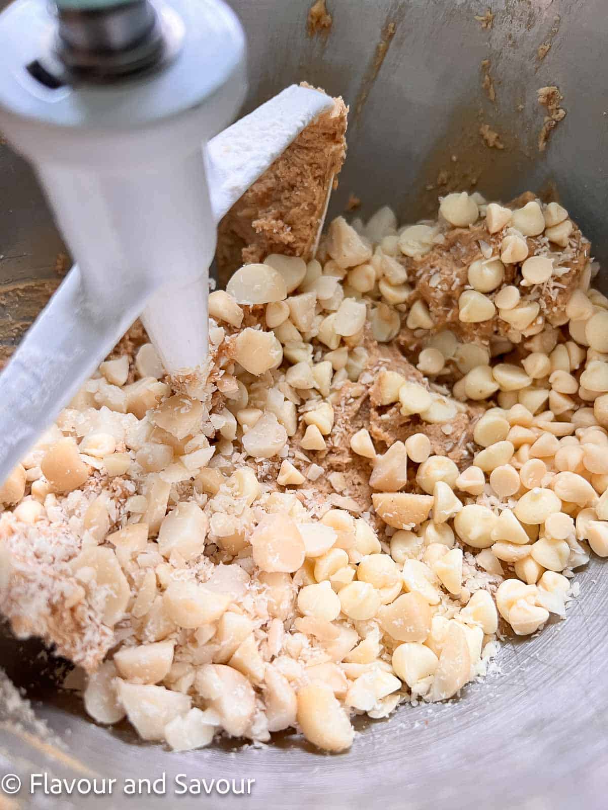 Adding chopped nuts and white chocolate chips to cookie dough in a stand mixer.