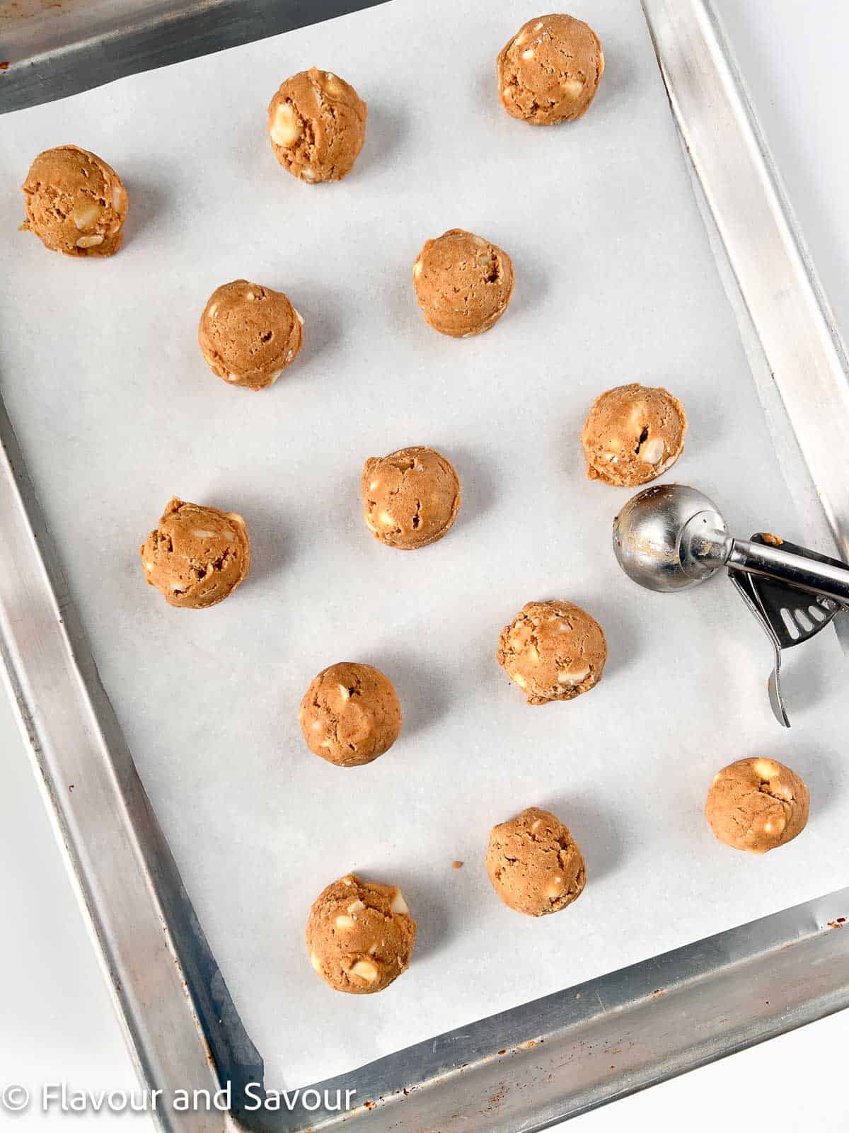Cookie dough balls on a baking sheet with a cookie scoop.