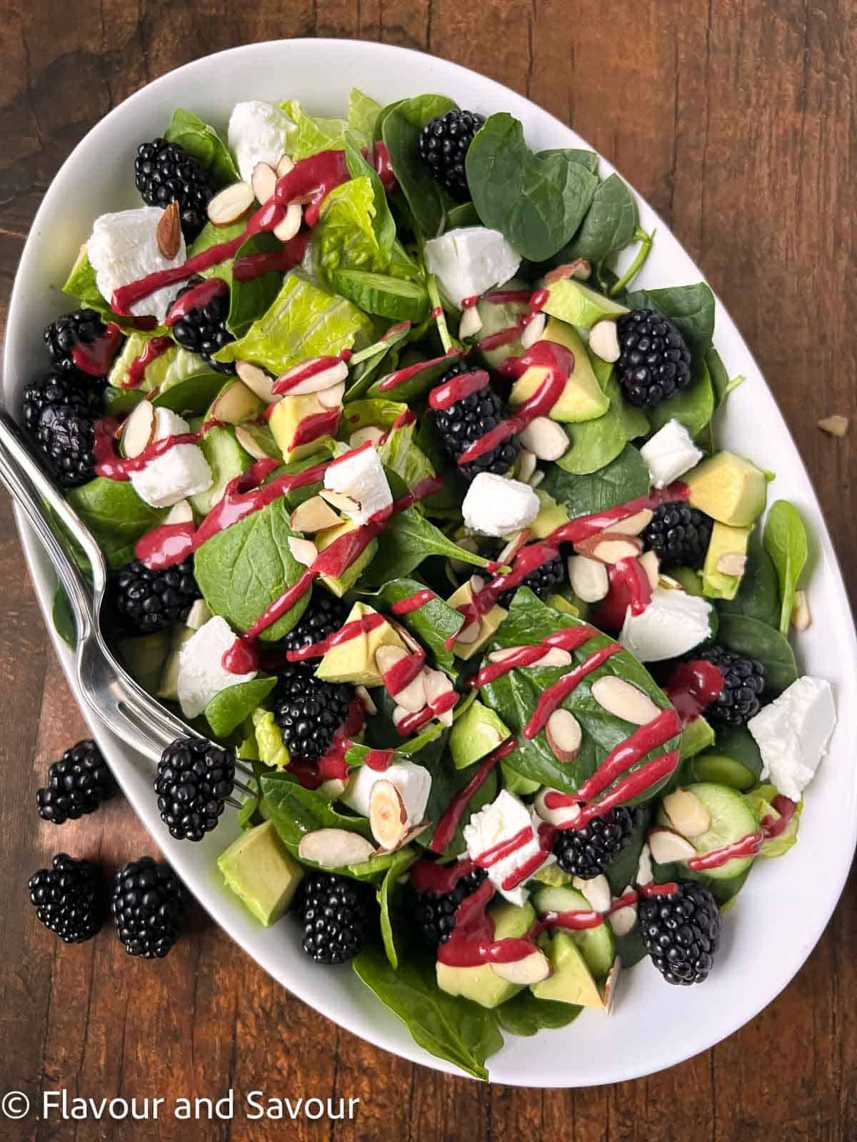 A large oval bowl with blackberry spinach salad with blackberry balsamic dressing.