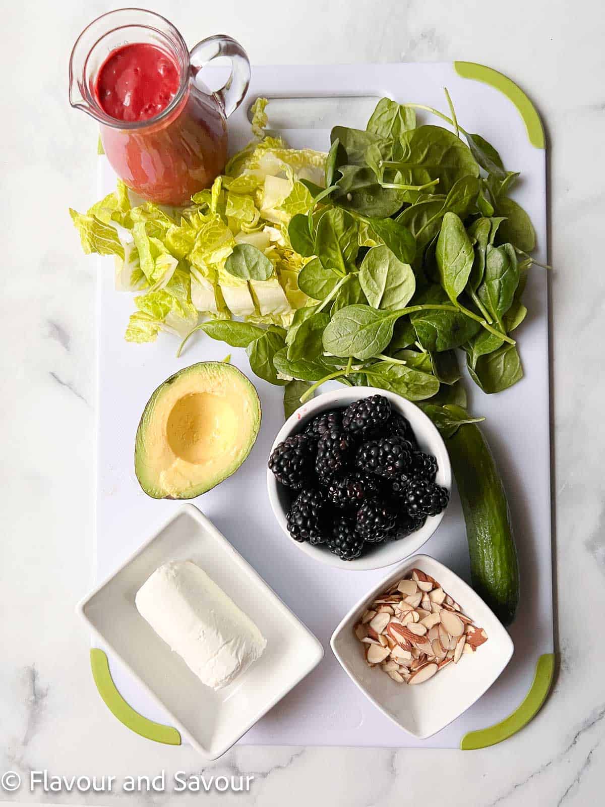 Ingredients for blackberry spinach salad: blackberry dressing, romaine, spinach, avocado, blackberries, cucumber, goat cheese, and toasted flaked almonds.