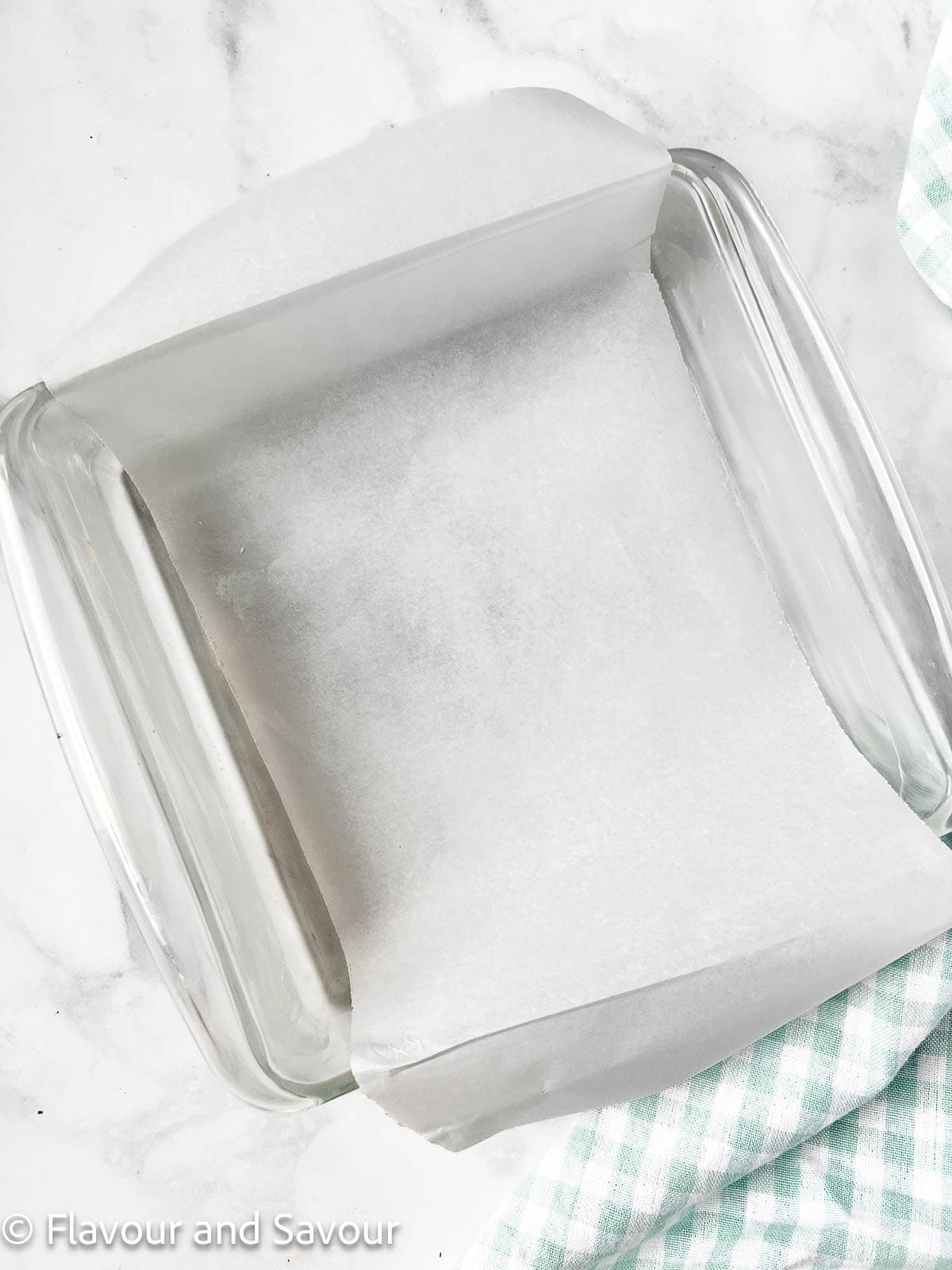 An 8-inch square glass baking pan lined with parchment paper.