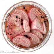 Pickled shallots in a jar with peppercorns.