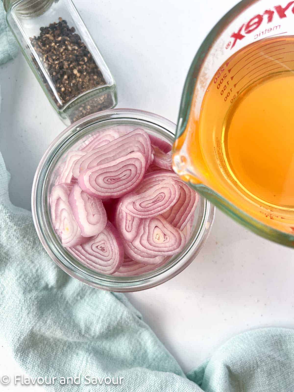 Hot pickling brine in a Pyrex measuring cup poured into a jar of sliced shallots.