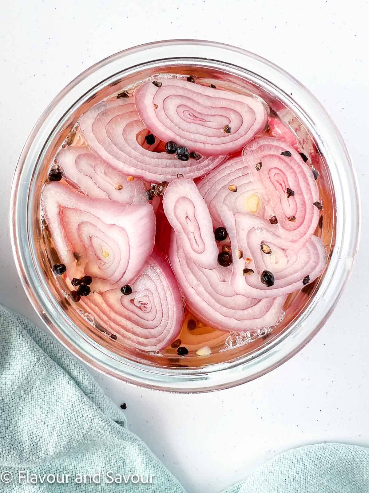 Sliced shallots with brine and peppercorn seeds in a Weck jar.