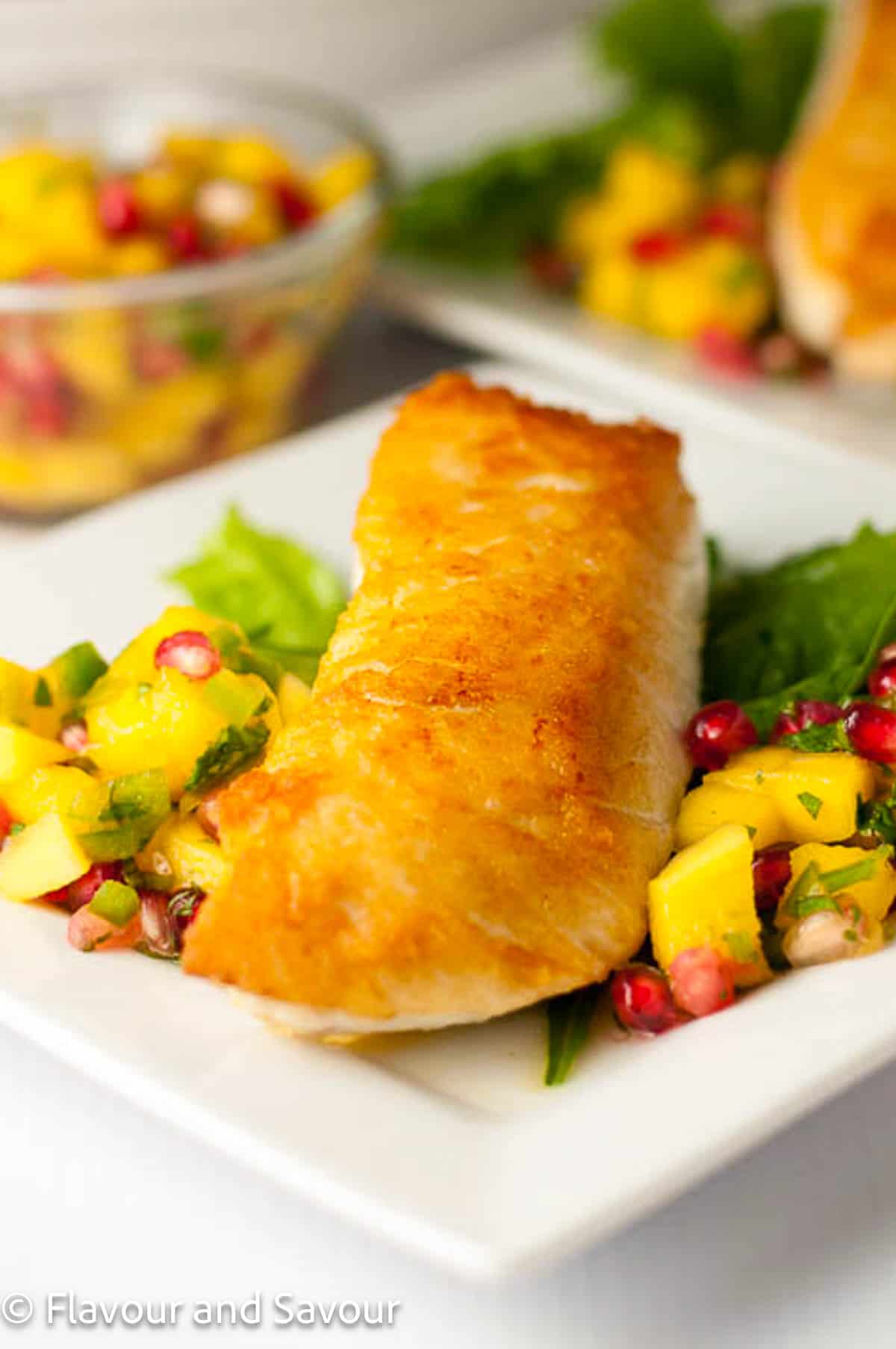 Salt and pepper crusted halibut fillet on a white plate with mango-pomegranate salsa.