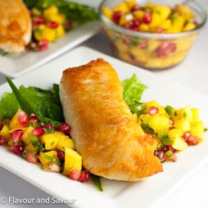 A crusted halibut fillet on a plate with mango-pomegranate salsa.