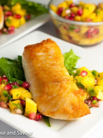 A crusted halibut fillet on a plate with mango-pomegranate salsa.
