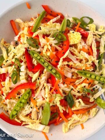 A bowl of Thai-style coleslaw with Napa cabbage, carrots red bell pepper, sugar snap pea pods and green onions.