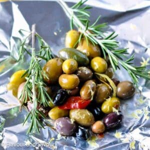 Mixed olives in small pile on a sheet of aluminum foil with sprgis of rosemary.